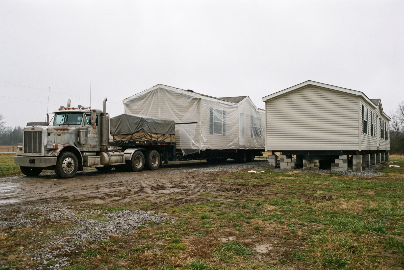 Half of a manufactured home on a transport trailer beside the half already set